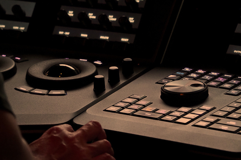 Hand operating a professional video editing console with trackballs, knobs, and buttons, representing DVD Your Memories’ Video Tribute Service in Southern California, where photos, video clips, and audio are skillfully edited together into personalized tribute videos.