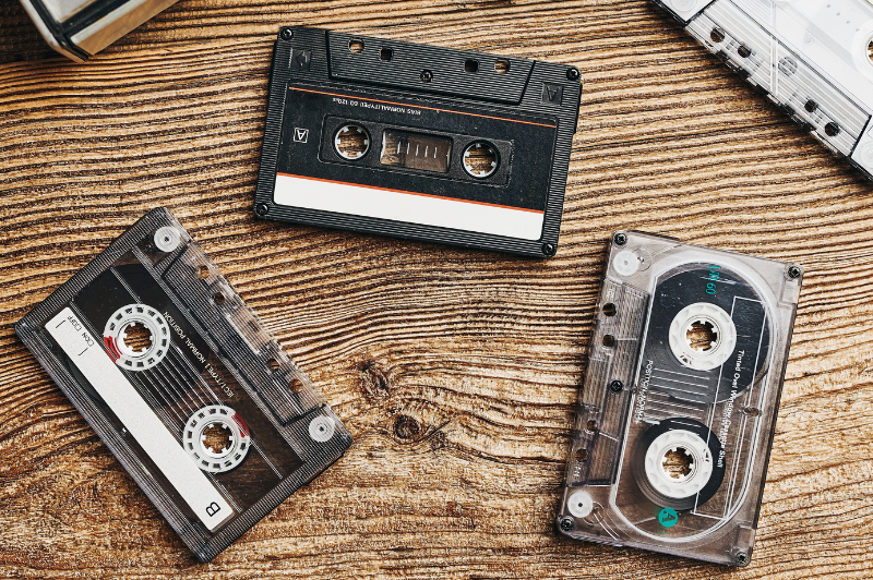Three vintage audio cassette tapes on a wooden table, representing audio transfer and digitization services by DVD Your Memories in Southern California.