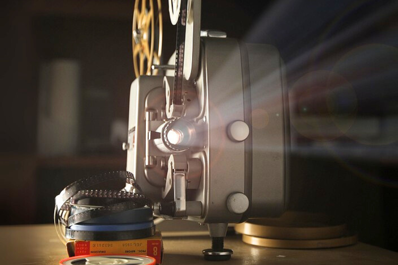 Vintage film projector with reels and film strips on a table, representing film transfer and digitization services by DVD Your Memories in Southern California.