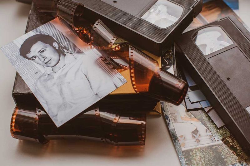 Black-and-white portrait photo, film negatives, and VHS tapes on a table, representing photo scanning services by DVD Your Memories in Southern California.