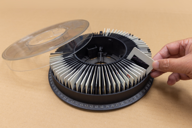 Hand placing a photographic slide into a round slide carousel, representing slide scanning and digitization services by DVD Your Memories in Southern California.
