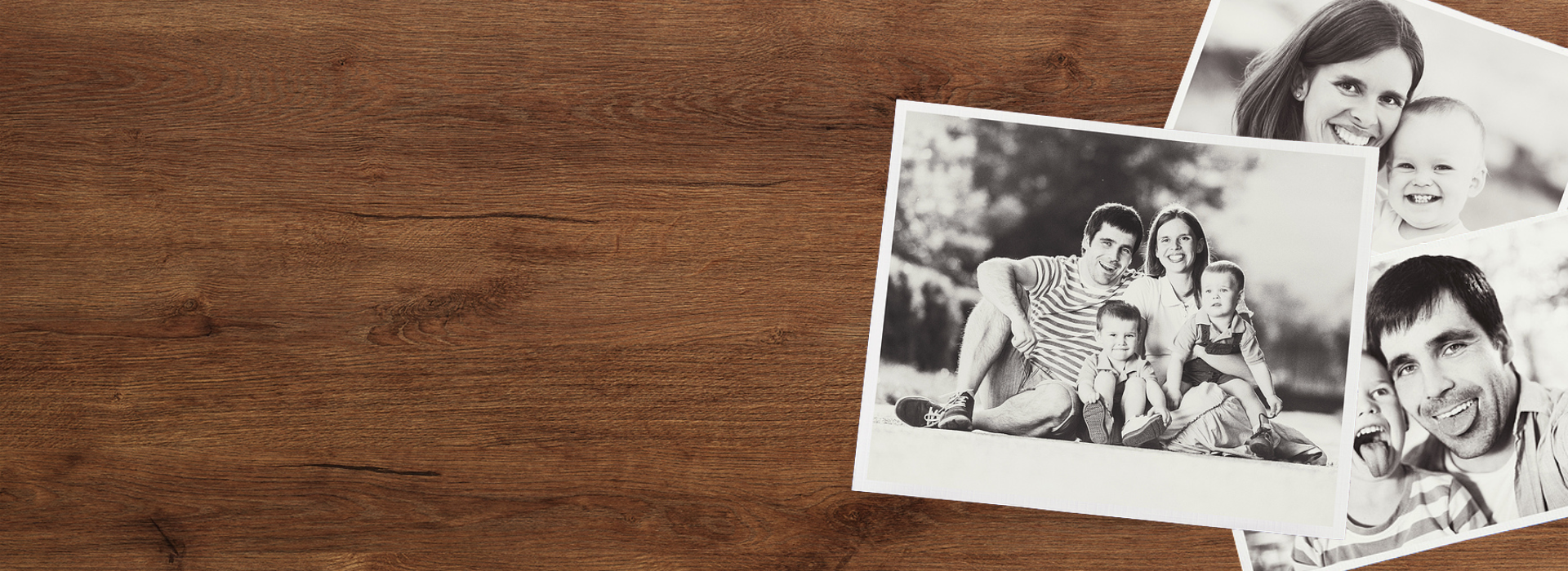 Black and white family photographs on wooden table representing convert to digital media by DVD Your Memories Orange County.