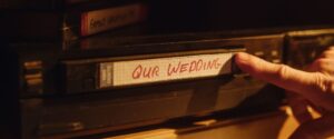 Someone pushes a VHS tape labeled "Our Wedding" into a player.
