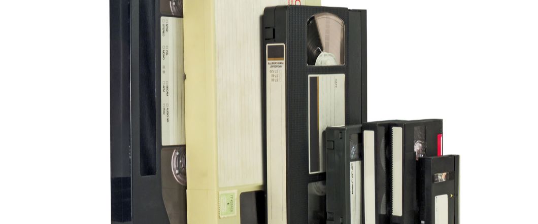 Stack of video tape formats including miniDV, VHS, VHS-C, and Hi8 standing upright
