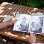 Two people looking over old black and white photos in an album while sitting outside at a table