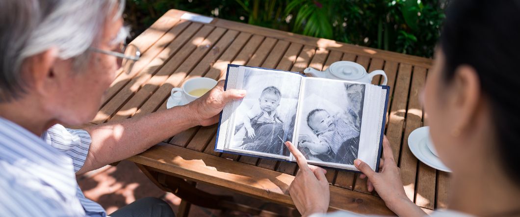 Two people looking over old black and white photos in an album while sitting outside at a table
