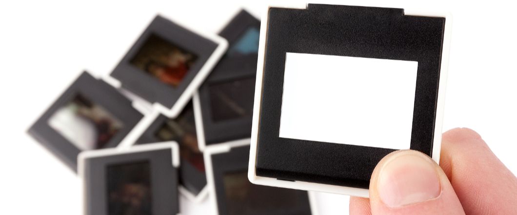 How To Convert 35mm Slides To Digital Without Losing Quality Hand holding a blank film slide above a pile of 35 mm slides