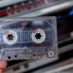 Hand holding an audio cassette, about to play the tape in a boombox