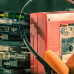 A cassette tape player next to a stack of cassettes, hooked up to a pair of headphones.
