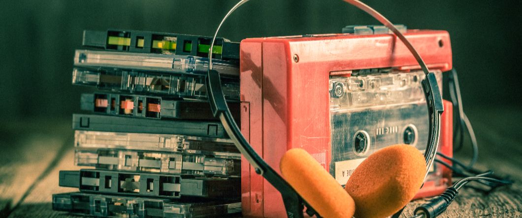 A cassette tape player next to a stack of cassettes, hooked up to a pair of headphones.